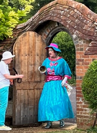 Granny Bean - panto dame arrives in gate wearing blue and pink dress with hat